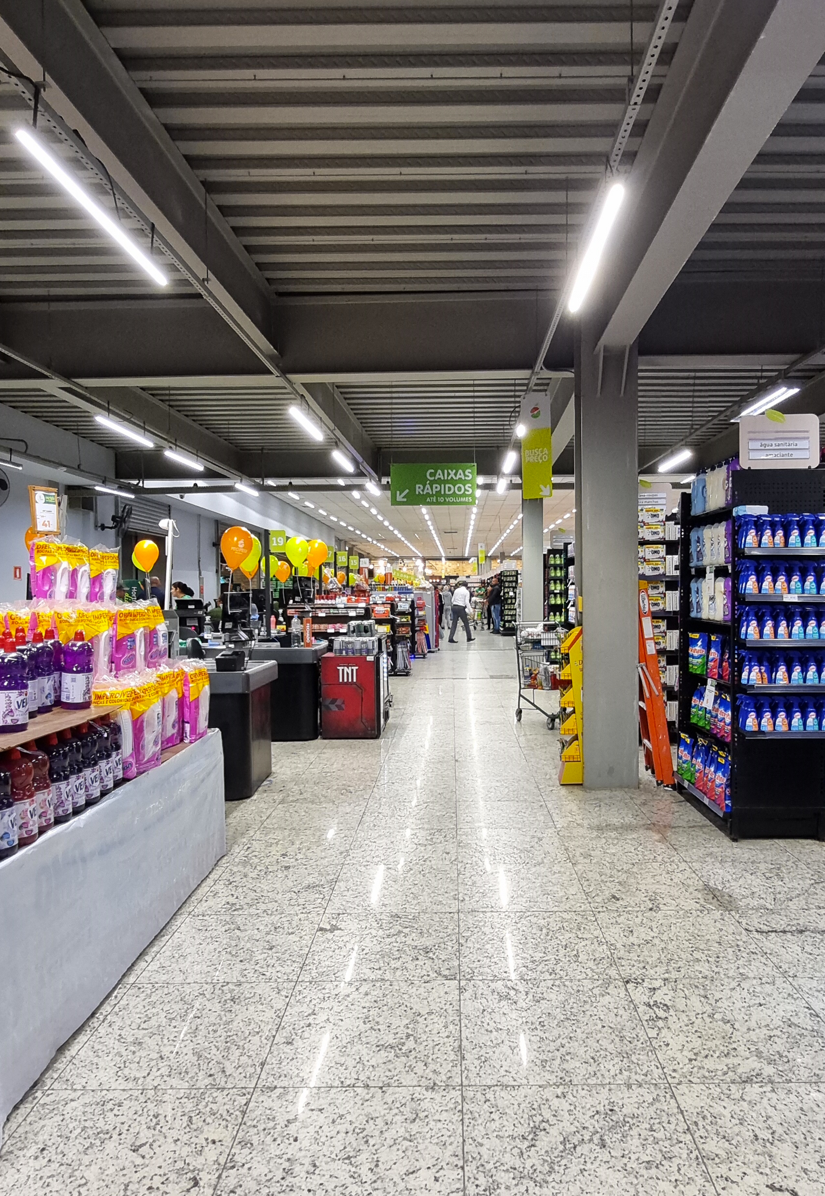 Projeto de iluminação comercial no corredor principal do supermercado Peg Pese Interlagos, com linhas contínuas de luz no teto industrial.